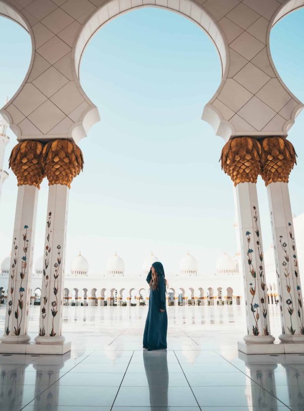 a woman standing in a courtyard with columns and gold and white pillars