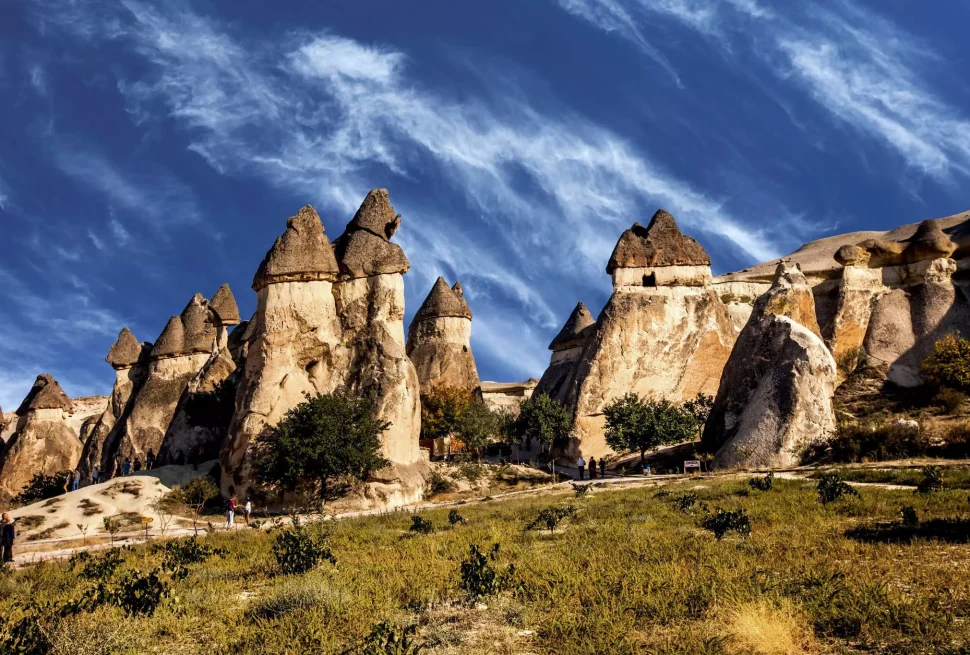 a group of people walking on a path in a grassy area with Cappadocia in the background