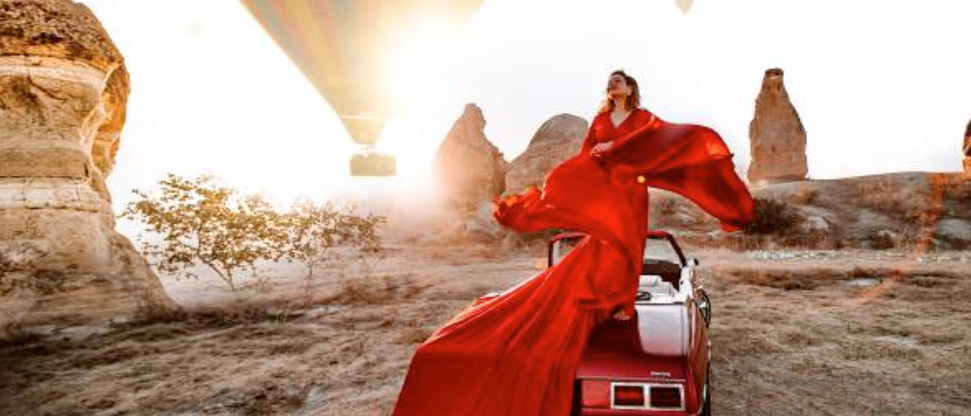 a woman in a red dress on a car with hot air balloons in the background