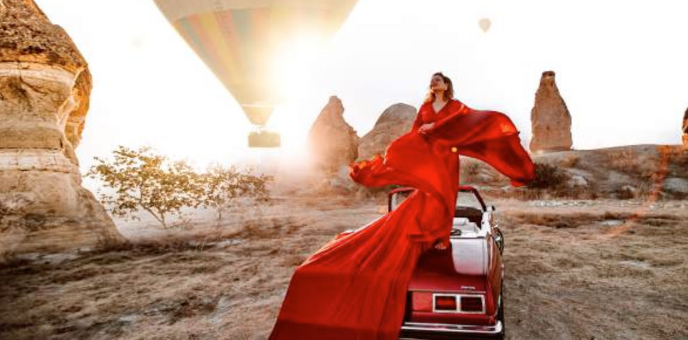 a woman in a red dress on a car with hot air balloons in the background