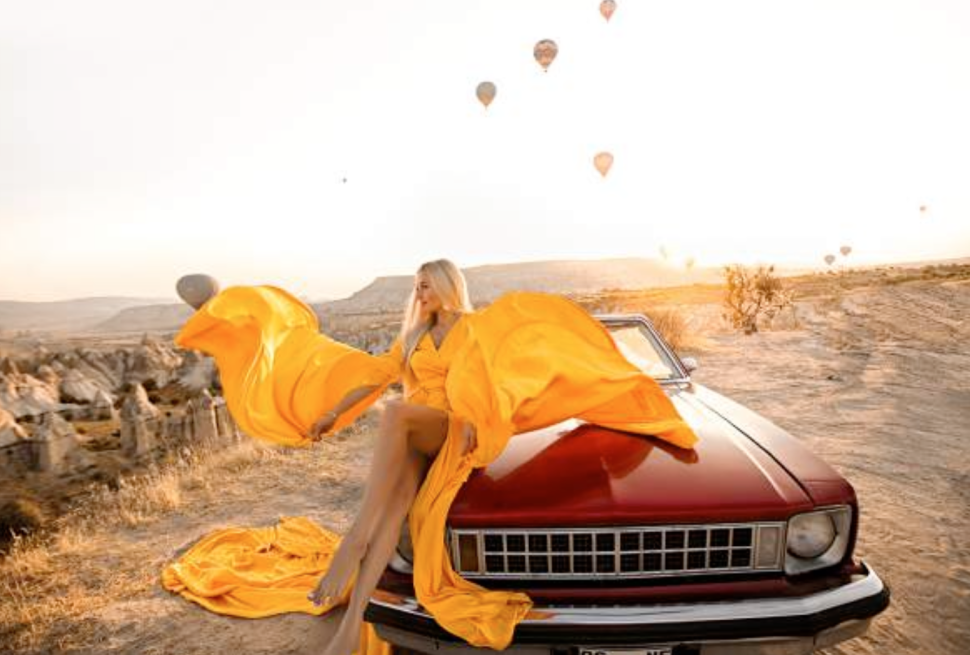 a woman sitting on a car with hot air balloons in the background