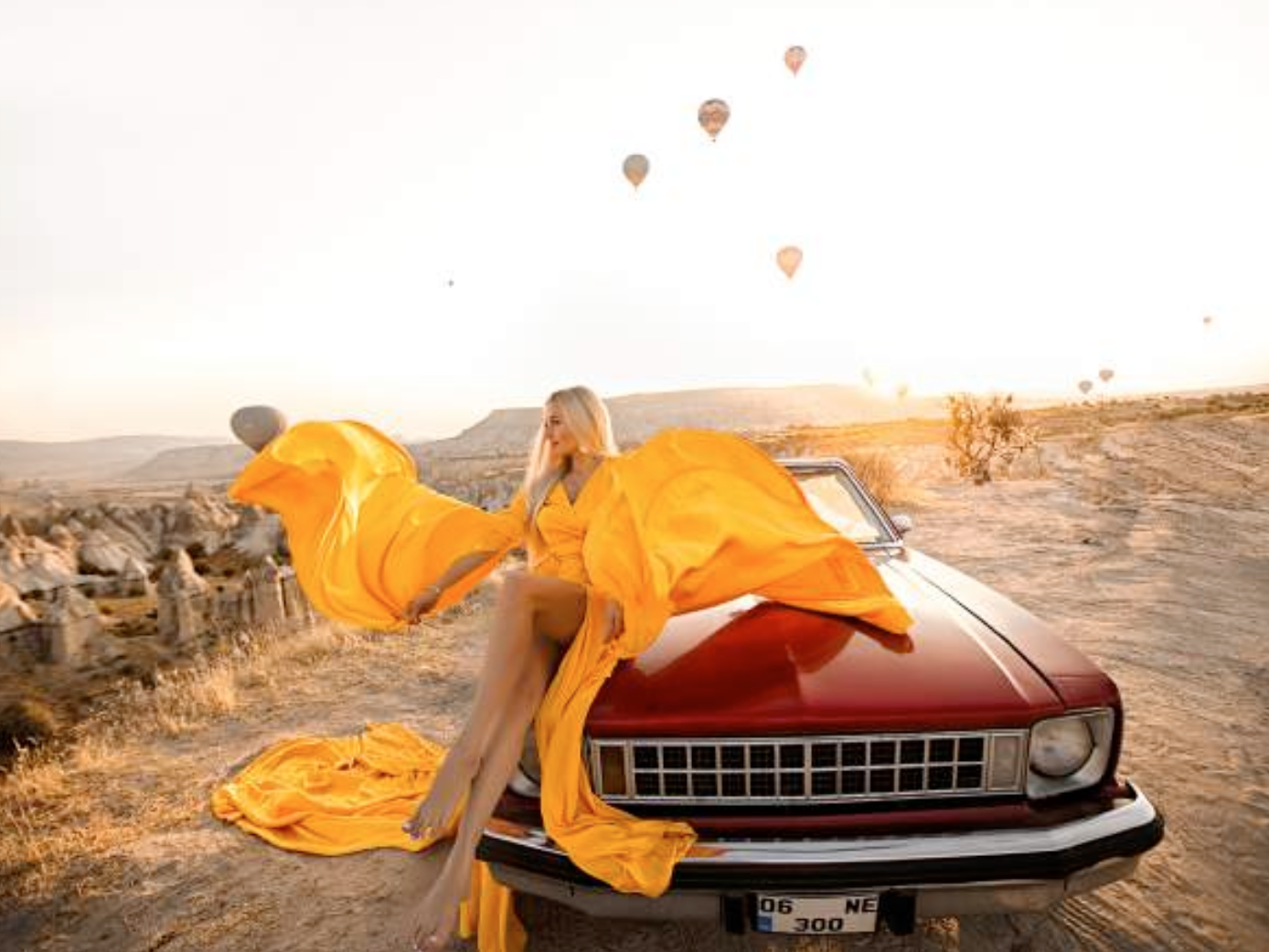 a woman sitting on a car with hot air balloons in the background